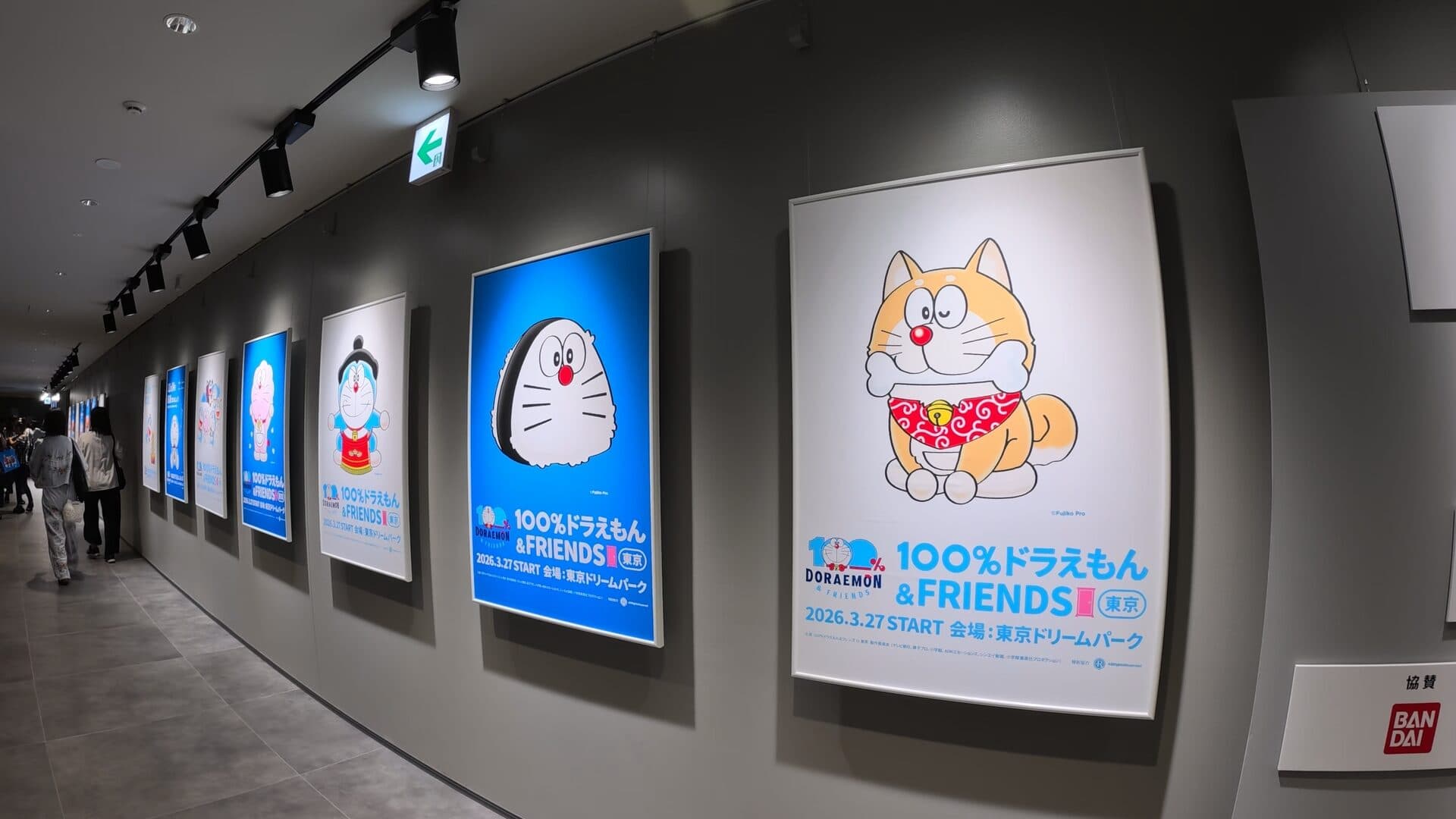 Framed posters along the curve, the Dorami poster dated 2026.3.27 START, and a Bandai sign.